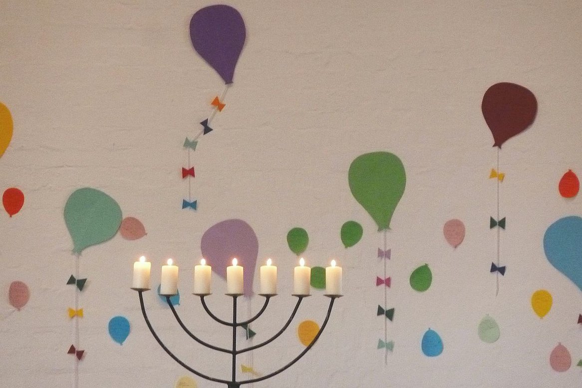 Zettel in Form von Luftballons an der Altarwand, davor siebenarmiger Leuchter