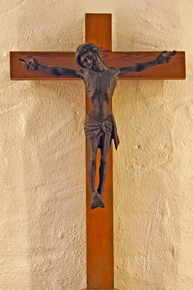 Gekreuzigter aus altem dunklem Eichenholz an einfachem Kreuz aus Kiefernholz vor verputzter Altarwand