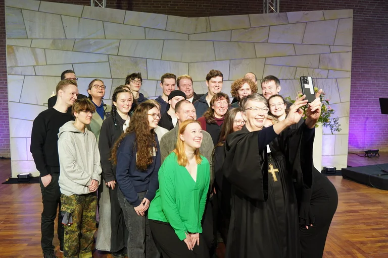 Eine Bischöfin macht ein Selfie mit einer großen Gruppe Menschen in einer Kirche.